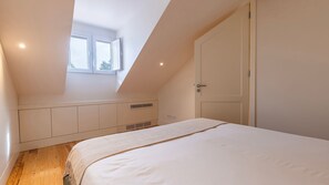Ein Schlafzimmer mit schrägem Dach, einem Fenster, einer Tür und integrierten Stauraumlösungen.