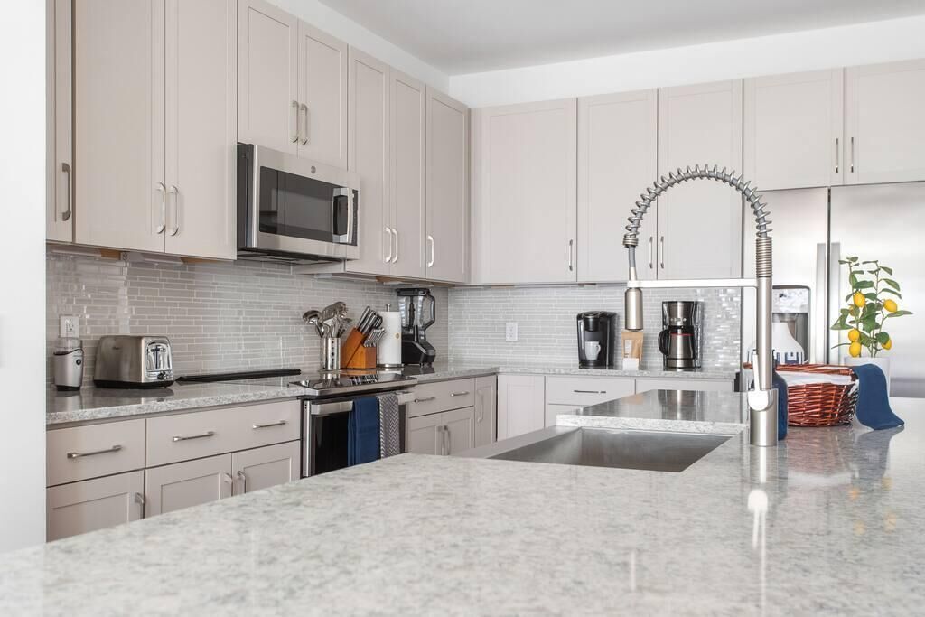A modern kitchen with light-colored cabinets, a stainless steel sink, a microwave, and a unique curved faucet.