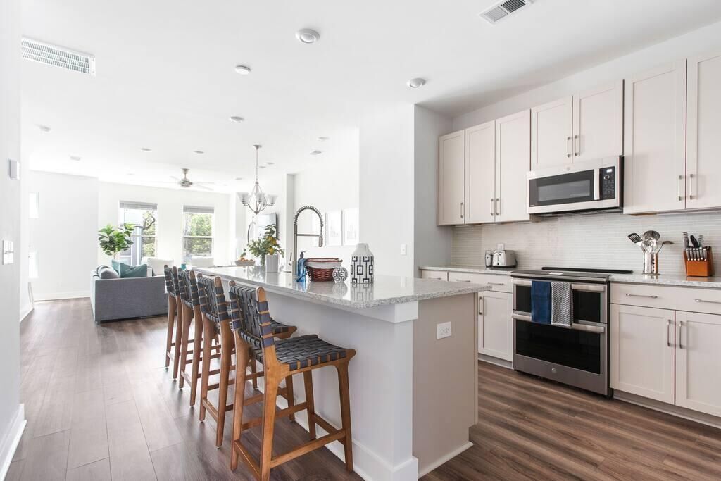 A modern kitchen with white cabinets, a central island with bar stools, stainless steel appliances, and a view to the dining area.