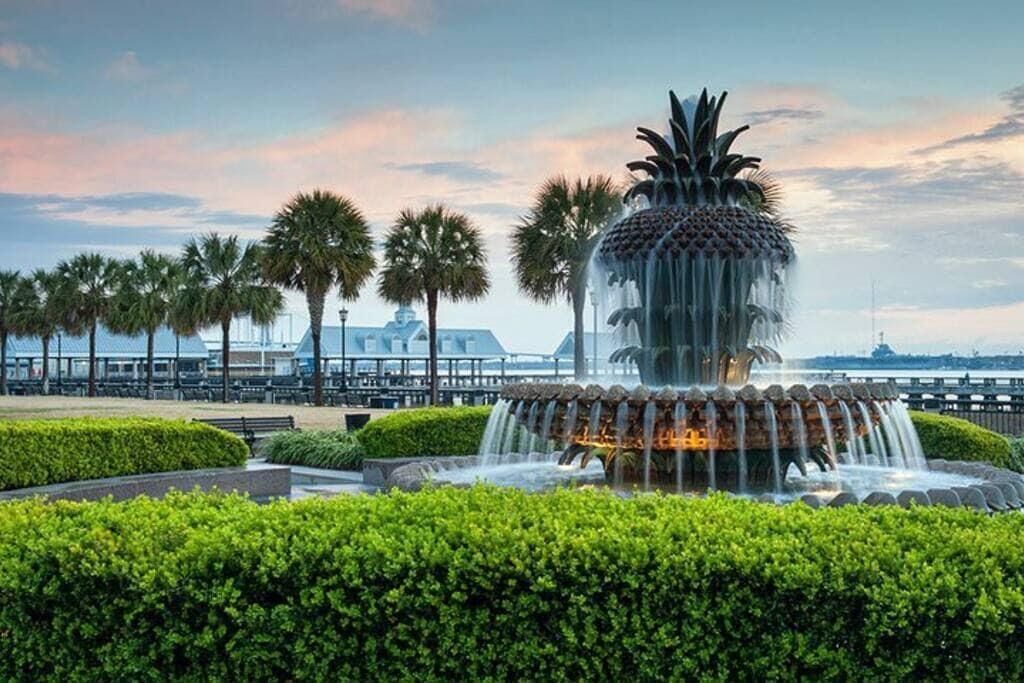 A fountain with a pineapple design surrounded by well-manicured bushes and palm trees.
