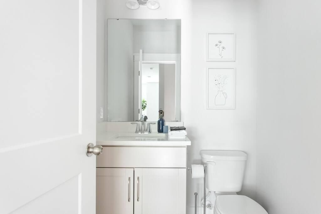 Un baño blanco con lavamanos, espejo e inodoro. Hay cuadros enmarcados en la pared.