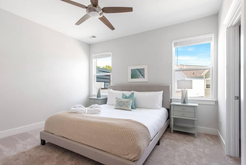 A bedroom with a bed, nightstands, a ceiling fan, and a window with a view.