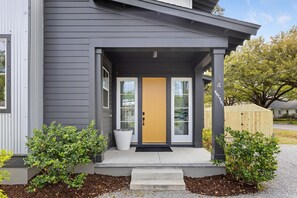 A modern house with a gray exterior, a yellow front door, and a small porch with steps leading to the entrance. - Music Manor-3-king Beds-pool-mins To Beach & DT (Mount Pleasant)