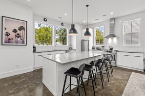 A modern kitchen with a large island, bar stools, pendant lights, and a view of the outdoors. - Music Manor-3-king Beds-pool-mins To Beach & DT (Mount Pleasant)