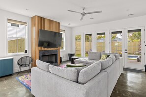 A modern living room with a sectional sofa, a flat-screen TV, a fireplace, and a ceiling fan. - Music Manor-3-king Beds-pool-mins To Beach & DT (Mount Pleasant)