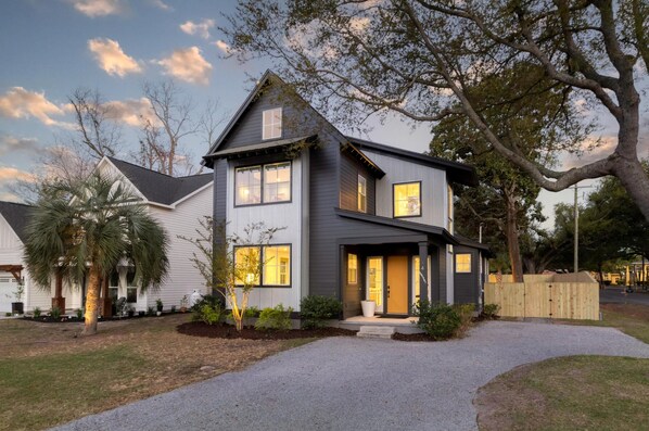 A two-story house with a front porch, a driveway, and a large tree. - Music Manor-3-king Beds-pool-mins To Beach & DT (Mount Pleasant)