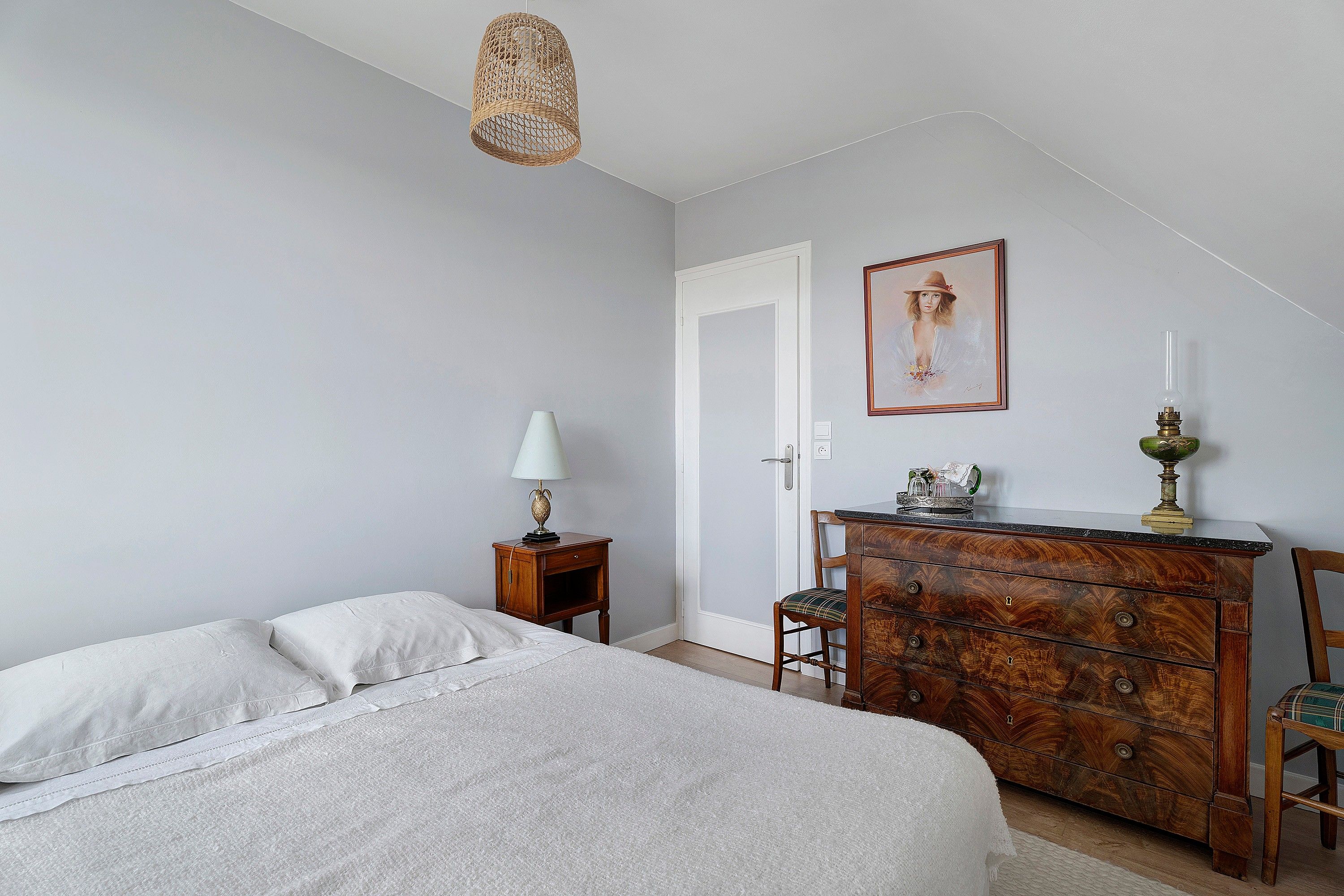 Une chambre à coucher avec un lit, une commode, une lampe, un tableau et un luminaire suspendu.