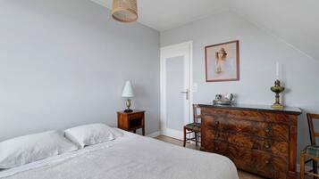 Une chambre à coucher avec un lit, une commode, une lampe, un tableau et un luminaire suspendu.