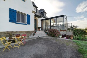 A house with a gravel patio, a small table with chairs, and a glass-enclosed balcony. - La Mainguy Guest Rooms (Ruca)