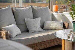 A wicker sofa with grey cushions and a lace pillow, accompanied by a small potted plant.