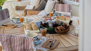 Een ronde houten tafel met een ontbijtsetting, inclusief brood, boter, jam en drankjes.