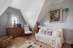 A cozy attic bedroom with a sloped ceiling, a wooden dresser, a white upholstered sofa, a floor lamp, and a painting on the wall. - La Mainguy Guest Rooms (Ruca)