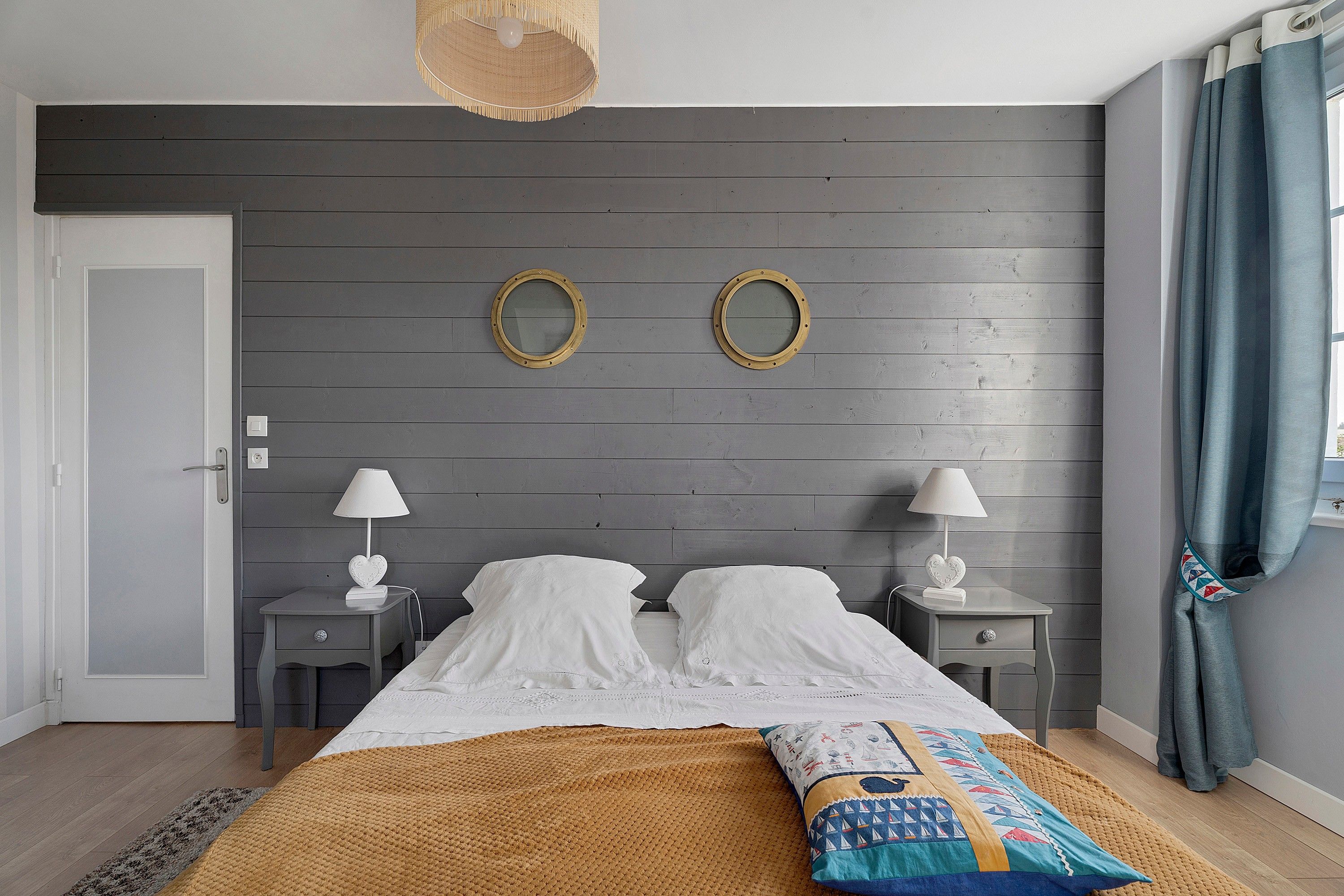 Une chambre à coucher avec un lit, deux tables de chevet, une lampe suspendue et une fenêtre avec des rideaux.