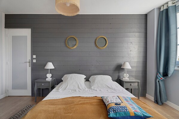 A bedroom with a bed, two bedside tables, a hanging light, and a window with curtains.