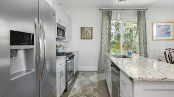 A modern kitchen with stainless steel appliances, a granite countertop, and a large window with curtains.