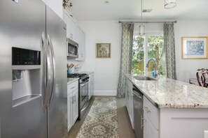 Uma cozinha moderna com eletrodomésticos de aço inoxidável, bancada de granito e uma grande janela com cortinas.