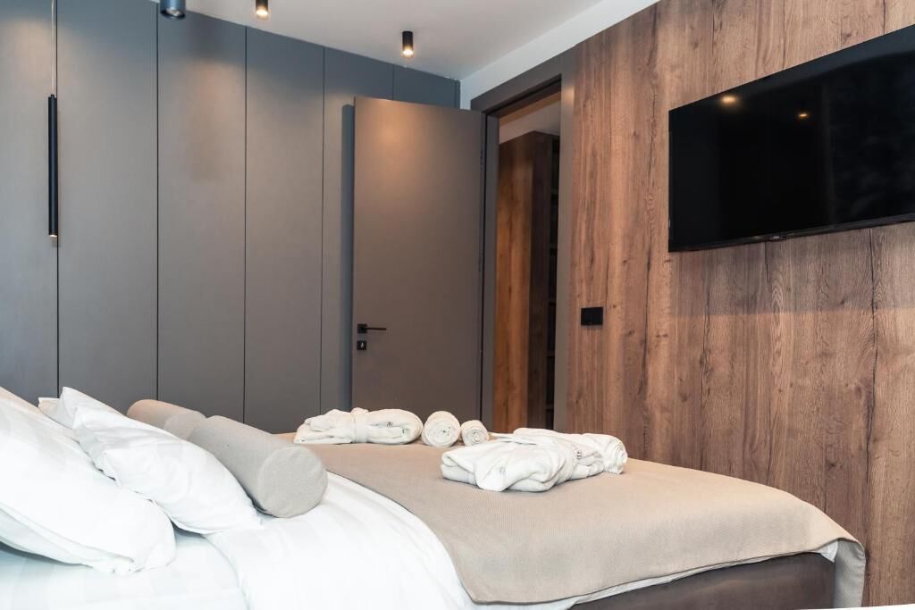 A modern hotel room with a bed, a flat-screen TV mounted on the wall, and a wooden panel accent.