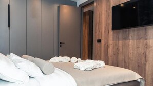 Una habitación de hotel moderna con una cama, un televisor de pantalla plana montado en la pared y un panel de madera decorativo.