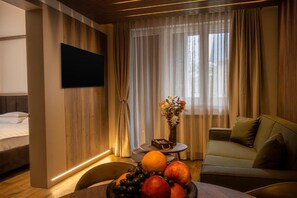 Ett hotellrum med en säng, en soffa, ett matbord med frukt, en vas med blommor och en tv som är monterad på väggen.