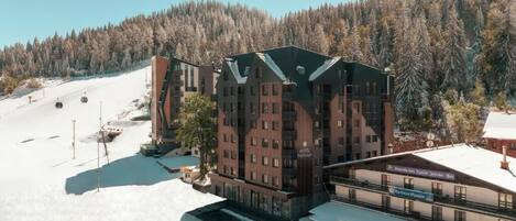 A multi-story hotel with a ski lift in the background, surrounded by a forested area.