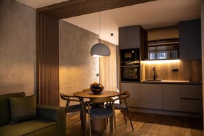 A modern kitchen with a dining area, including a round table with chairs, a hanging light fixture, and built-in appliances.