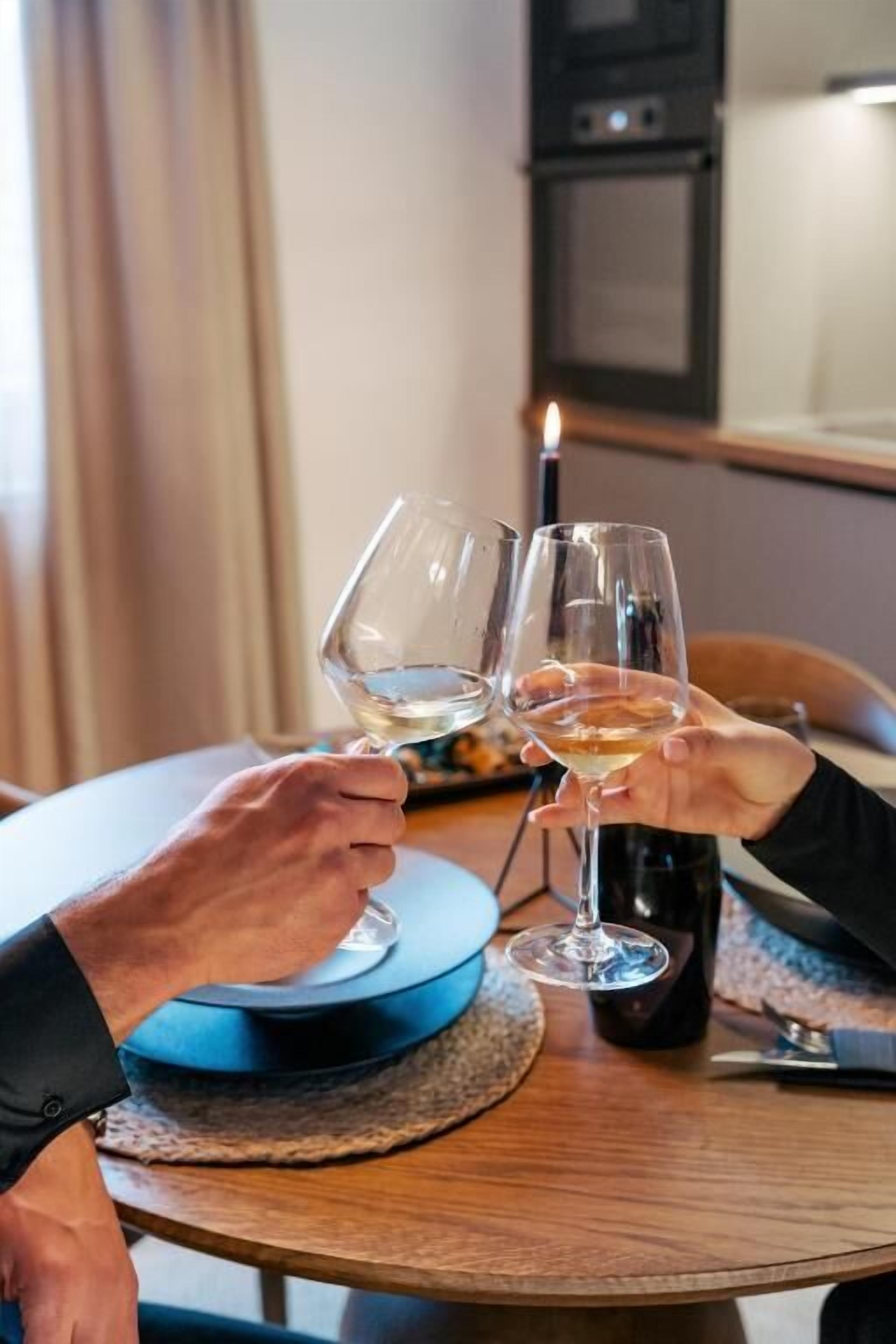 Two people toasting with wine glasses at a round table with a bottle of wine.