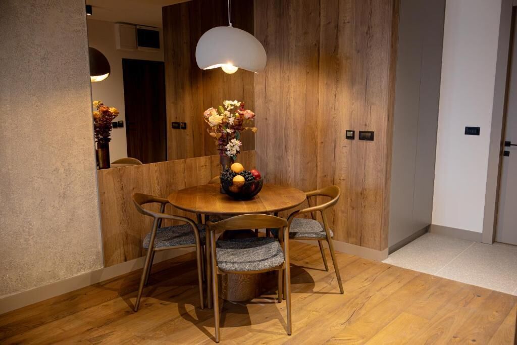 A dining area with a round table, four chairs, a vase with flowers, and a hanging light fixture.