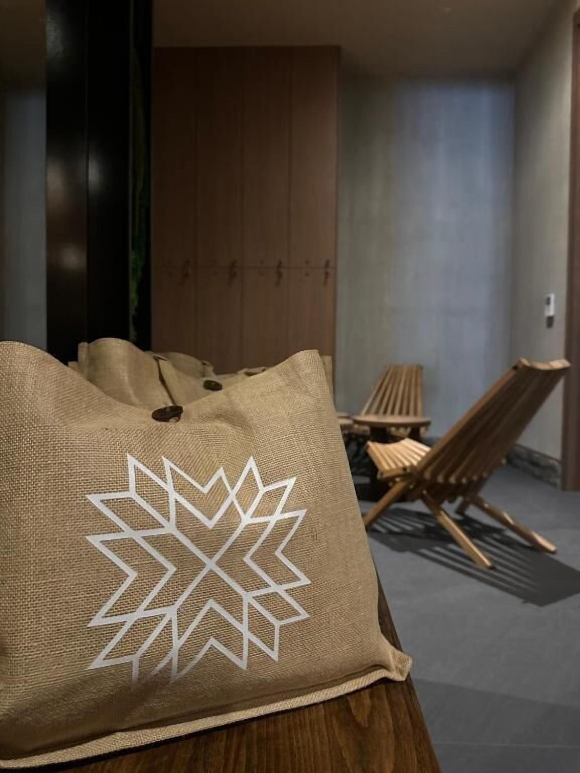 Une pièce avec un plancher en bois, un canapé marron, une chaise en bois et un coussin à motifs.