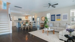 A spacious living area with a dining table, sofa, and a ceiling fan. A kitchen is visible in the background. - Happy Ours, Mins to Park Circle, Dtwn, CHS Beach (North Charleston)