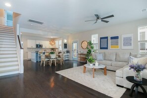 A spacious living area with a dining table, sofa, and a ceiling fan. A kitchen is visible in the background. - Happy Ours, Mins to Park Circle, Dtwn, CHS Beach (North Charleston)