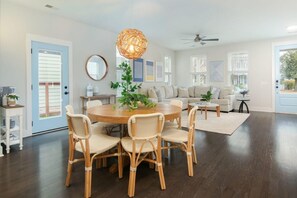 A spacious living room with a round dining table surrounded by wicker chairs, a ceiling fan, and a large window with blinds. - Happy Ours, Mins to Park Circle, Dtwn, CHS Beach (North Charleston)