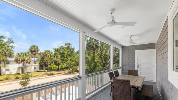 A covered outdoor area with a table and chairs, a ceiling fan, and a view of a pool and trees. - Jungle House-heated Pool-pet Friendly-luxury (Edisto Island)