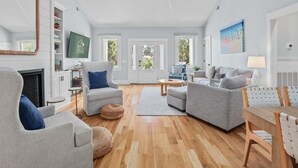 A spacious living room with a fireplace, grey sofas, a coffee table, and a dining area with a wooden table and chairs. - Jungle House-heated Pool-pet Friendly-luxury (Edisto Island)
