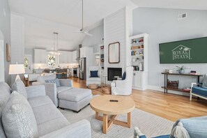 A spacious living area with a fireplace, a television displaying 'Royal Stays', and a kitchen in the background. - Jungle House-heated Pool-pet Friendly-luxury (Edisto Island)