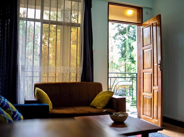 Una habitación con sofá, una mesa con un cuenco, una puerta y una ventana con cortinas.