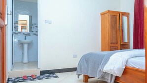 Ein Schlafzimmer mit Bett, einem Holzschrank, einem Badezimmer mit Waschbecken und einem Spiegel.