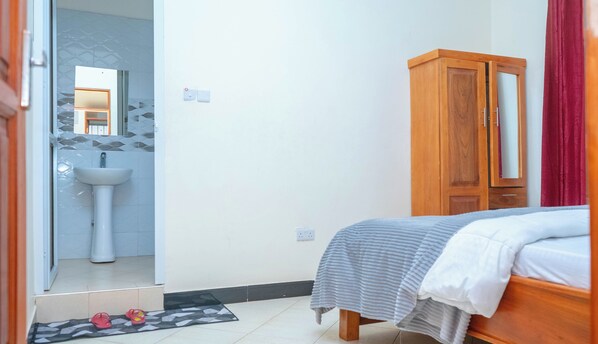Un dormitorio con cama, armario de madera, baño con lavamanos y espejo.