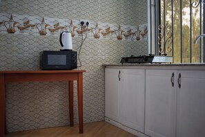 Una cocina con un microondas sobre una mesa de madera, una tetera y una ventana con reja de metal.