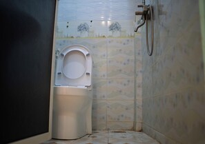 Et badeværelse med toilet, bruser og mønstrede fliser.