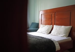 Una habitación de hotel con cabecera de madera, una cama con ropa de cama blanca y un sillón azul.