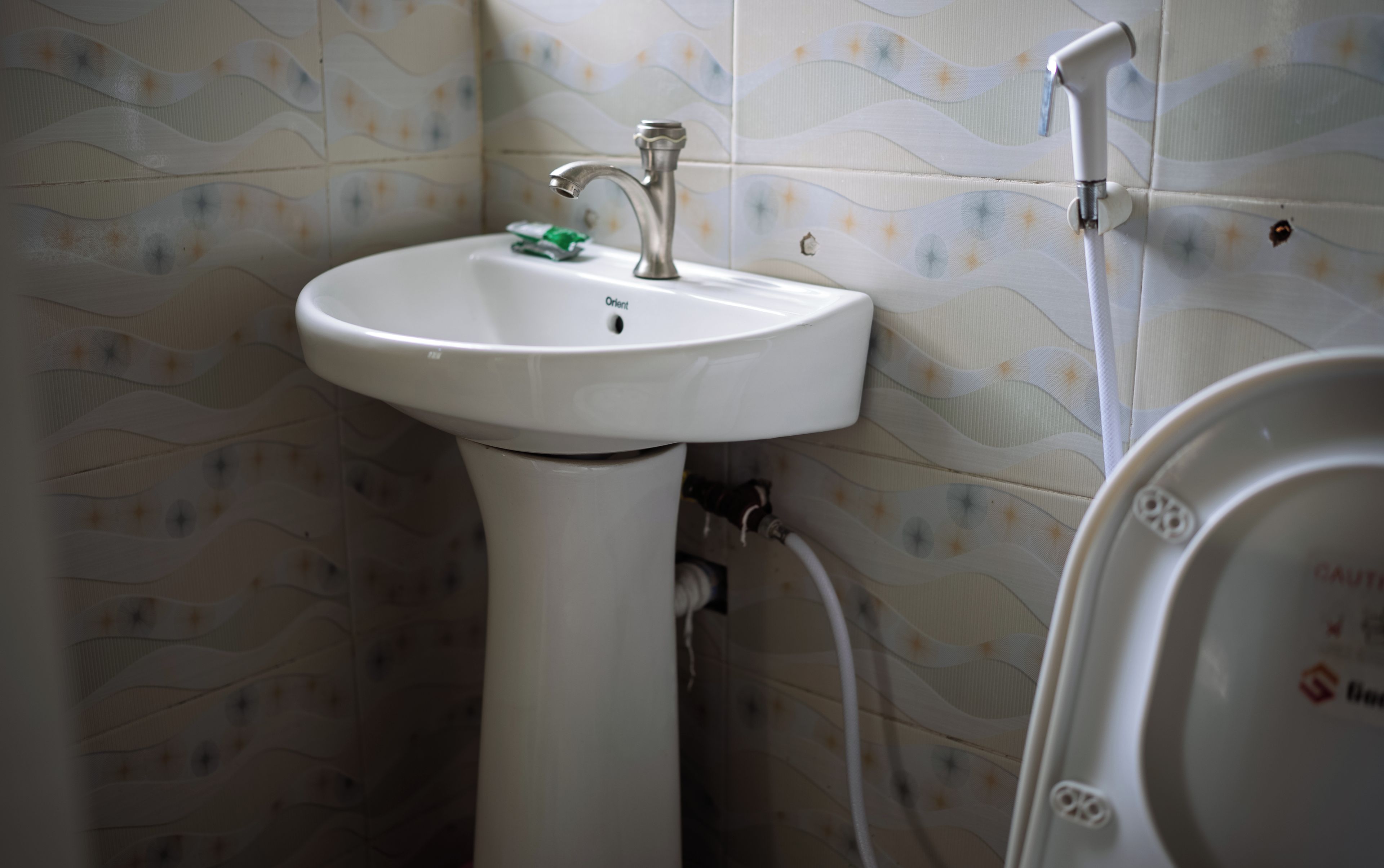A bathroom with a white pedestal sink, a faucet, and a toilet.