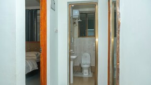 Ein kleines Badezimmer mit Toilette, Waschbecken und Dusche. Ein Bett ist im angrenzenden Raum zu sehen.