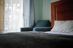 A bedroom with a bed, a chair, and a window with curtains. - Marvelous first floor 2-bedrooms apartments in Arusha perfect for your stay (Arusha)