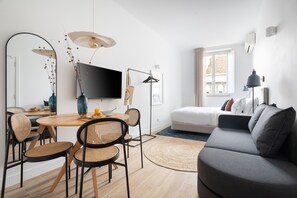 Uma sala de estar moderna com um sofá, uma mesa de jantar com cadeiras, uma televisão e uma janela com cortinas.