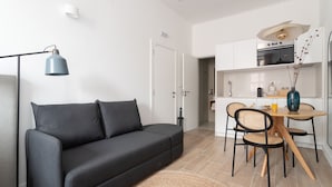 A modern living room with a sofa, a dining table with chairs, a lamp, and a kitchen area with cabinets and appliances. - Lapa Diplomatic Collection by Feel Lisboa (Lisbon)