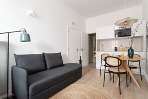 Uma sala moderna com sofá, mesa de jantar com cadeiras, luminária e área de cozinha com armários e eletrodomésticos.