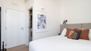 A bedroom with a white bed, a framed abstract painting, a bedside lamp, and a headboard with pillows. - Lapa Diplomatic Collection by Feel Lisboa (Lisbon)
