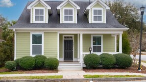 A two-story house with a front porch, a dark front door, and a small front yard with trimmed bushes. - The Jade, Park Circle, Mins to Dwtn and Beaches (North Charleston)