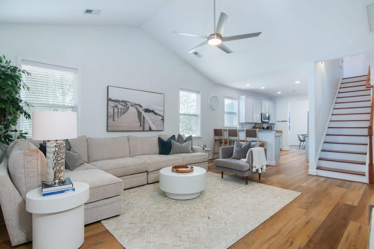 A spacious living room with a beige sofa, a white coffee table, and a modern ceiling fan.
