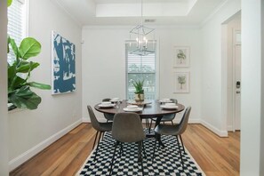 Un comedor con una mesa redonda, sillas, un tapete con estampado blanco y negro, una lámpara colgante y cuadros en la pared.